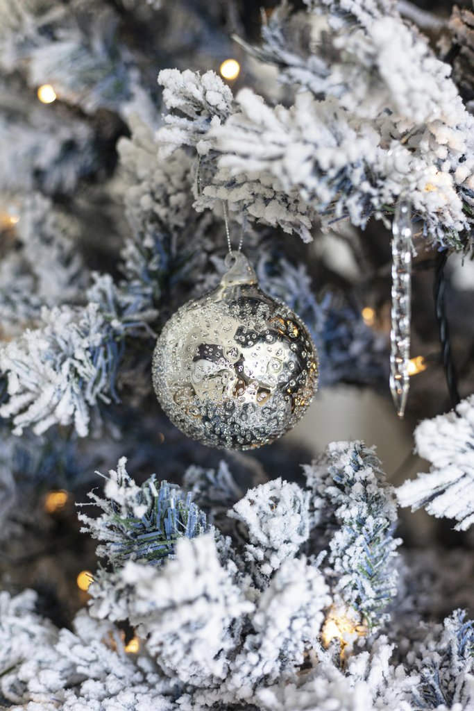 craveiro_ pics - Silver bauble on frosted Christmas tree with warm lights, evoking winter holiday charm.