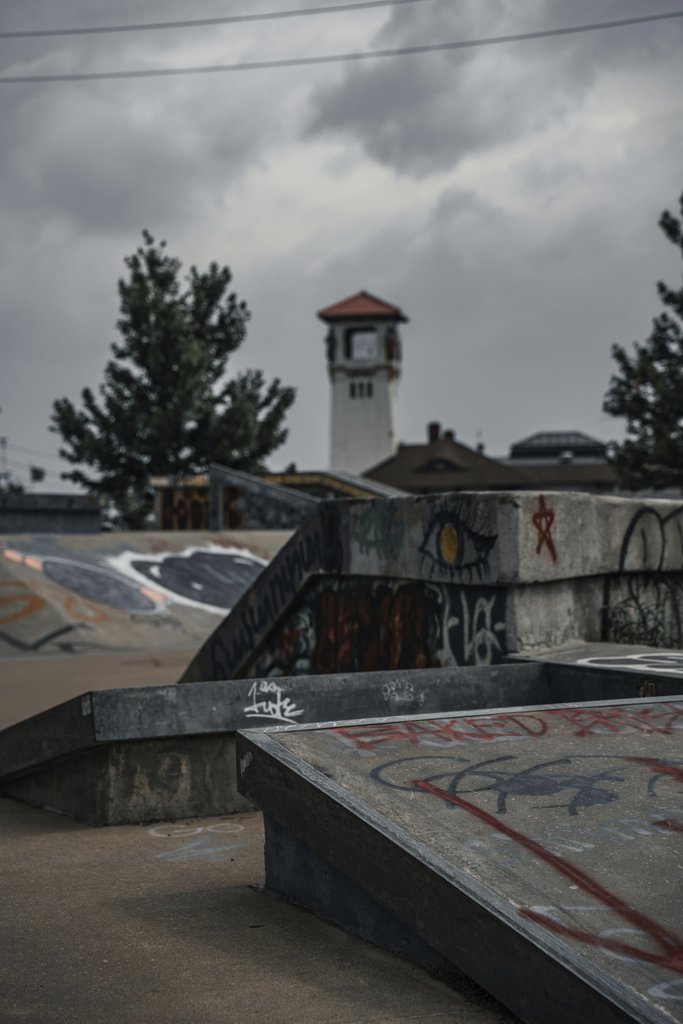 Connor McManus - Discover a graffiti-covered skatepark under an overcast sky, with a classic clock tower backdrop.