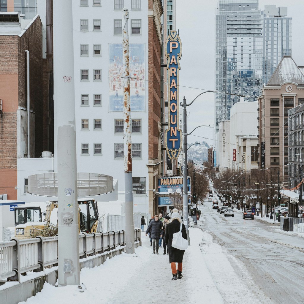 Qingju Wen - Snowy Seattle city street with Paramount Theatre in winter, showcasing urban architecture and passersby.