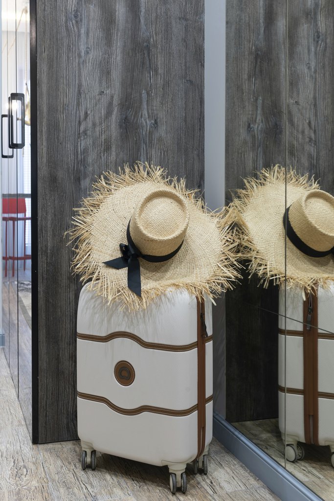 Max Vakhtbovycn - A chic straw hat resting on a suitcase in a contemporary hotel hallway, ready for travel.