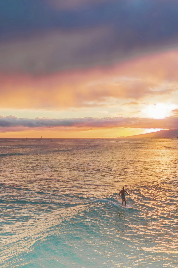 Jess Loiterton - A lone surfer embraces the setting sun with vibrant skies on the ocean. Perfect for themes of adventure and nature.