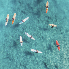 Jess Loiterton - Aerial shot of surfers resting on surfboards in clear blue ocean, a perfect summer water sport scene.