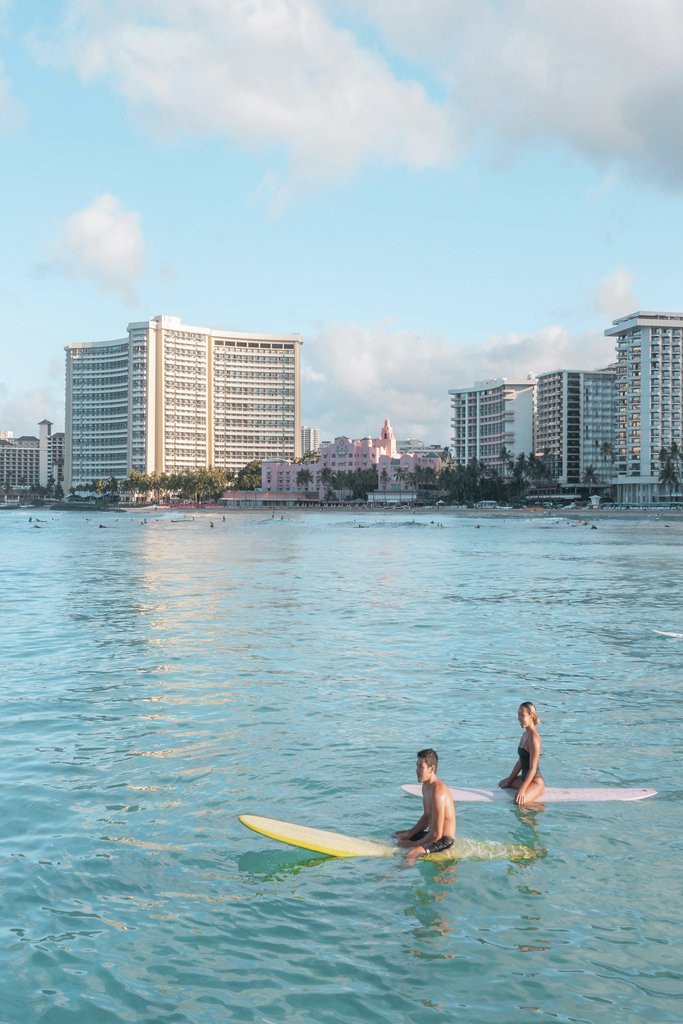 Jess Loiterton - Two surfers enjoying a sunny day on the ocean near coastal skyscrapers.