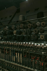 Melike Baran - Photo of old textile machine with spools indoors, dark industrial ambiance.