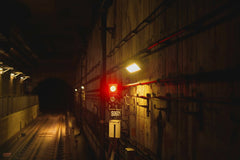 YIYANG LIU - A dimly lit subway tunnel featuring a bold red signal light casting shadows on the gritty walls.
