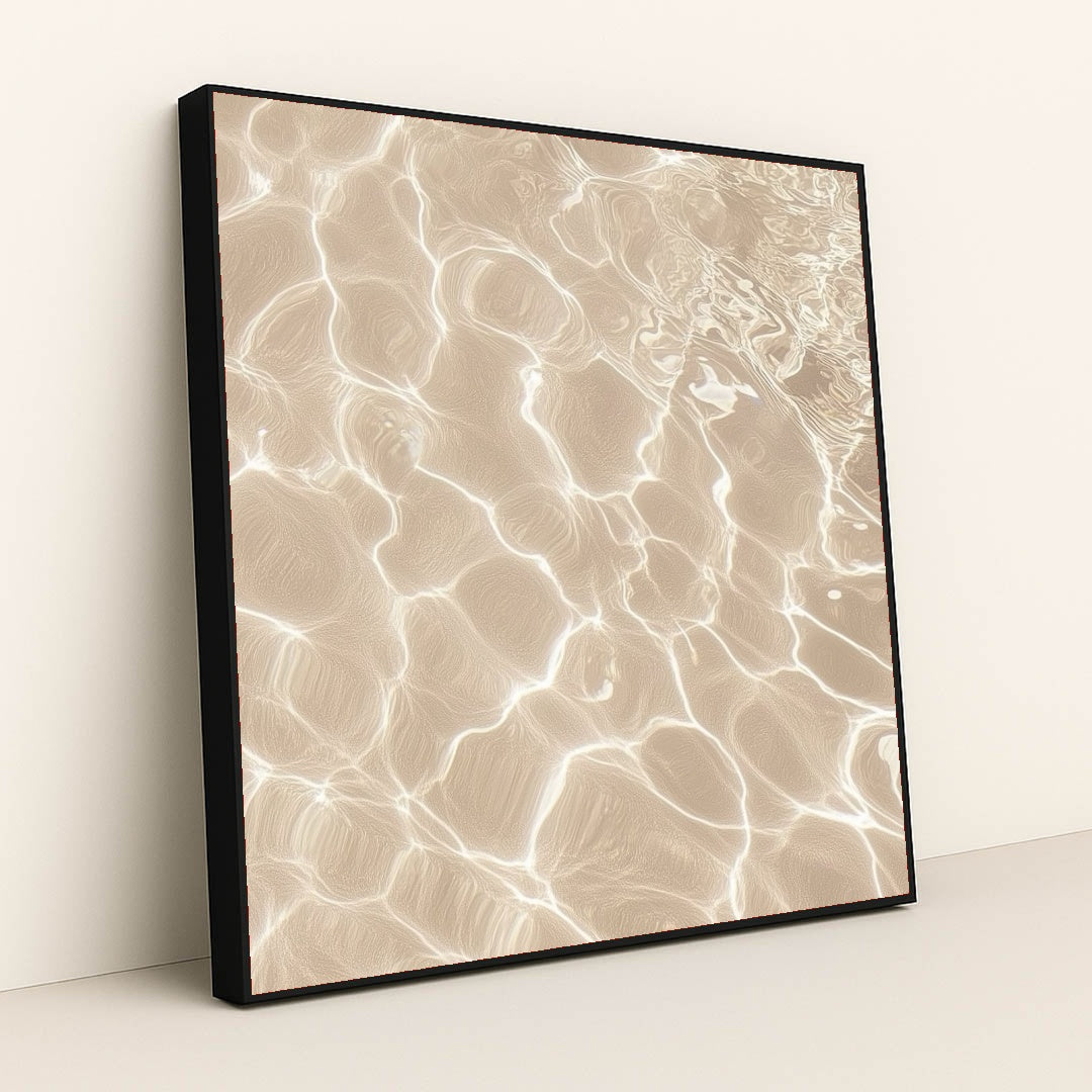 This artwork features sunlight reflecting on shallow sand and water, creating bright abstract patterns, in a black frame.