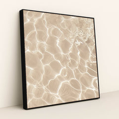 This artwork features sunlight reflecting on shallow sand and water, creating bright abstract patterns, in a black frame.