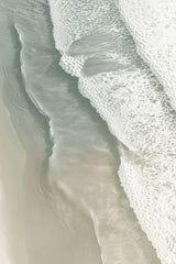 This artwork shows soft ocean waves washing onto smooth sand from above.