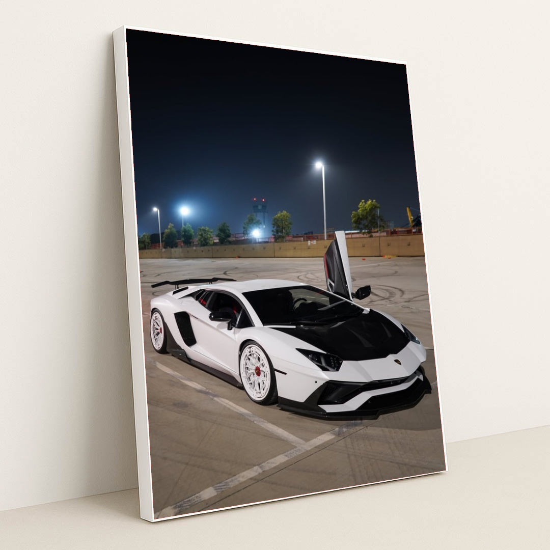 This photo shows a white Lamborghini Aventador with white wheels and an open door parked under streetlights at night, in a white frame.