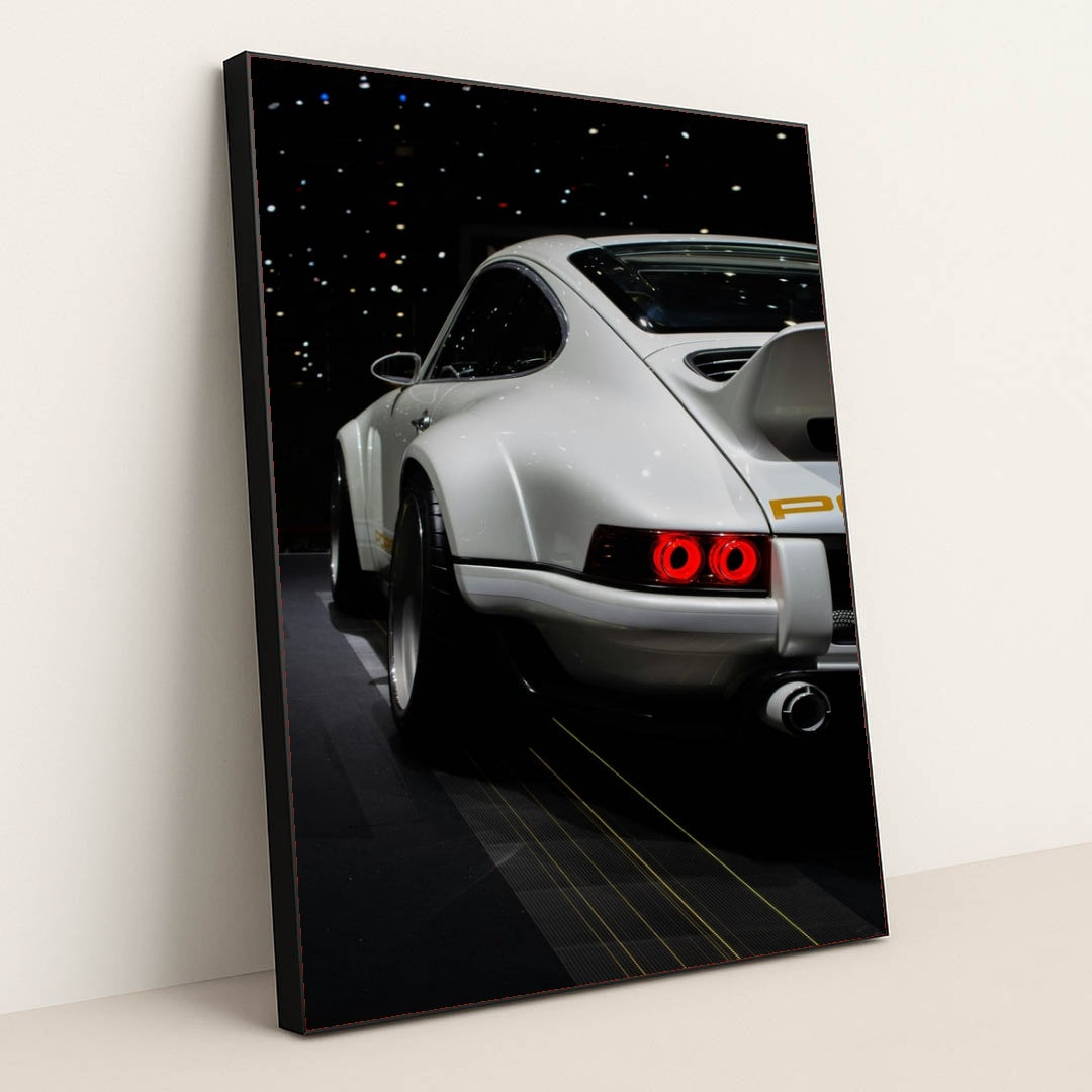 This photo shows the rear of a white Porsche sports car with a large wing, illuminated taillights, and starry reflections, in a black frame.