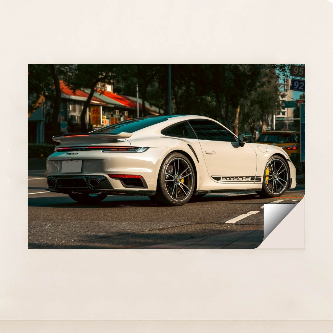 This photo shows a white Porsche 911 Turbo sports car parked on a street with black Porsche side decals, minimalist unframed style.