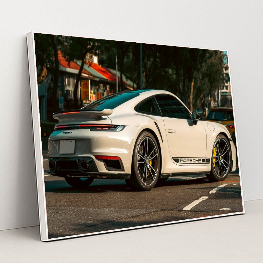 This photo shows a white Porsche 911 Turbo sports car parked on a street with black Porsche side decals, in a white frame.