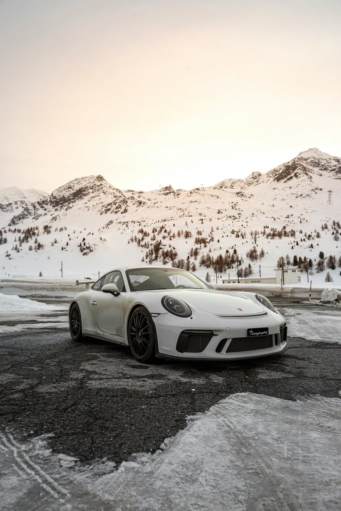Porsche 911 GT3 in Alpine Stillness, a white car on icy pavement with snow-capped peaks and golden light.