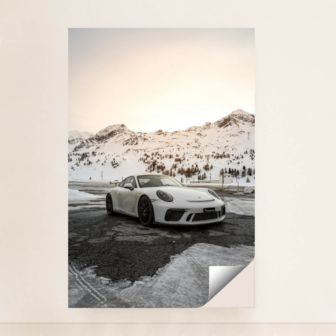 This photo shows a white Porsche sports car parked on a snow-covered mountain road at sunset, minimalist unframed style.