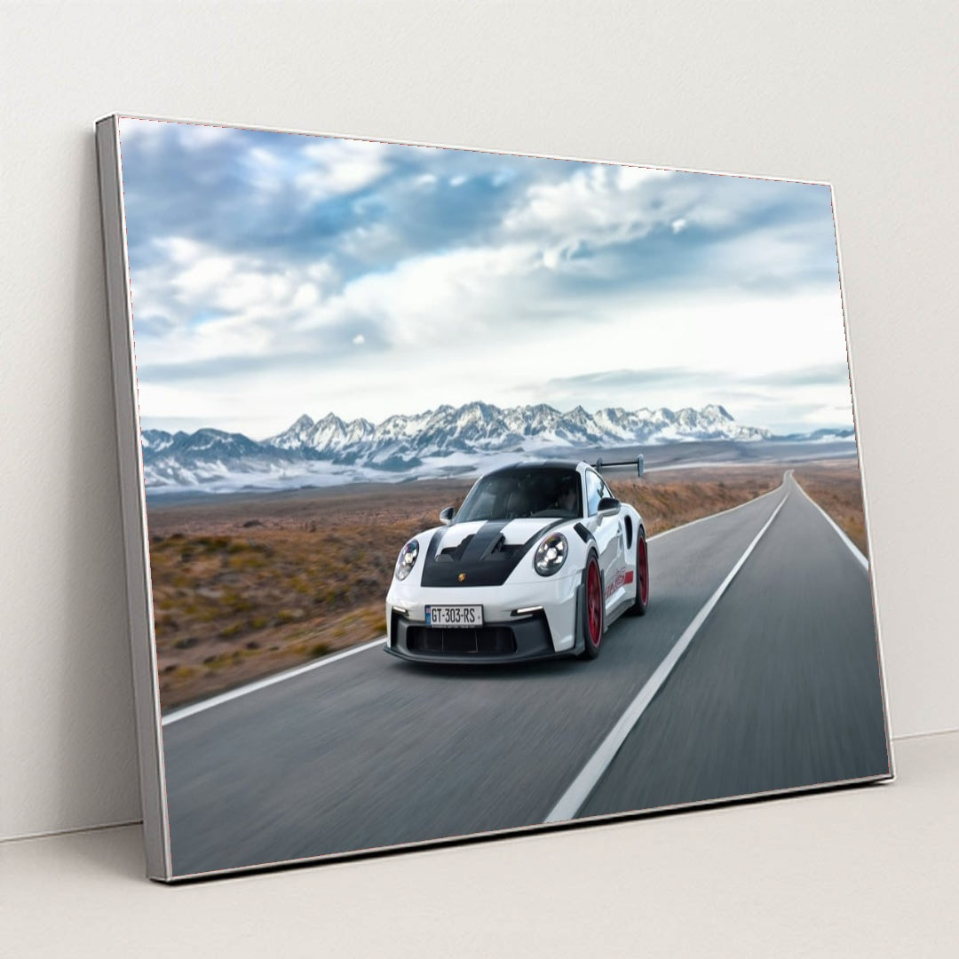 This photo shows a white Porsche 911 GT3 RS with red wheels driving quickly on an open desert highway with mountains in the background, in a silver frame.