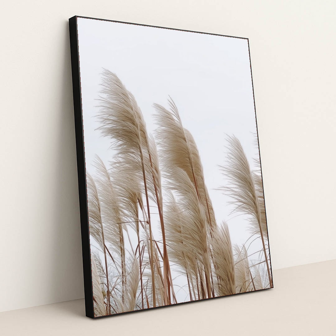 This artwork features tall beige pampas grass stems against a pale sky, in a black frame.