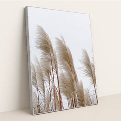 This artwork features tall beige pampas grass stems against a pale sky, in a silver frame.
