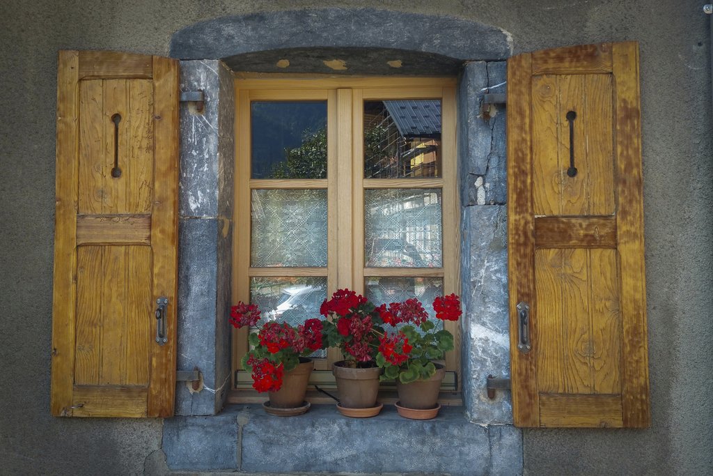 Paweł Kosmala - A rustic wooden window adorned with red geraniums in clay pots against a stone wall.