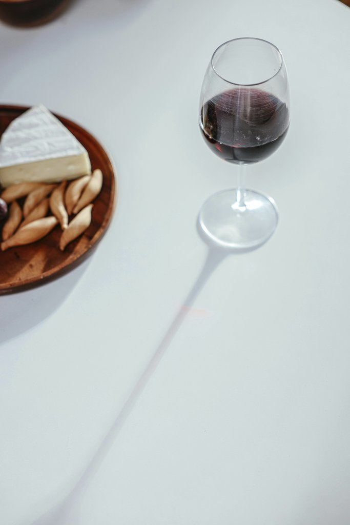 Cup of  Couple - A glass of red wine beside a cheese platter, casting a soft shadow on a white table.