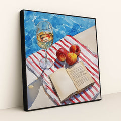 This artwork features a wine glass, peaches, and an open book on a striped towel beside a pool, in a black frame.