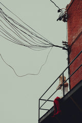 Connor McManus - A woman stands alone on an urban balcony under tangled power lines, conveying solitude.