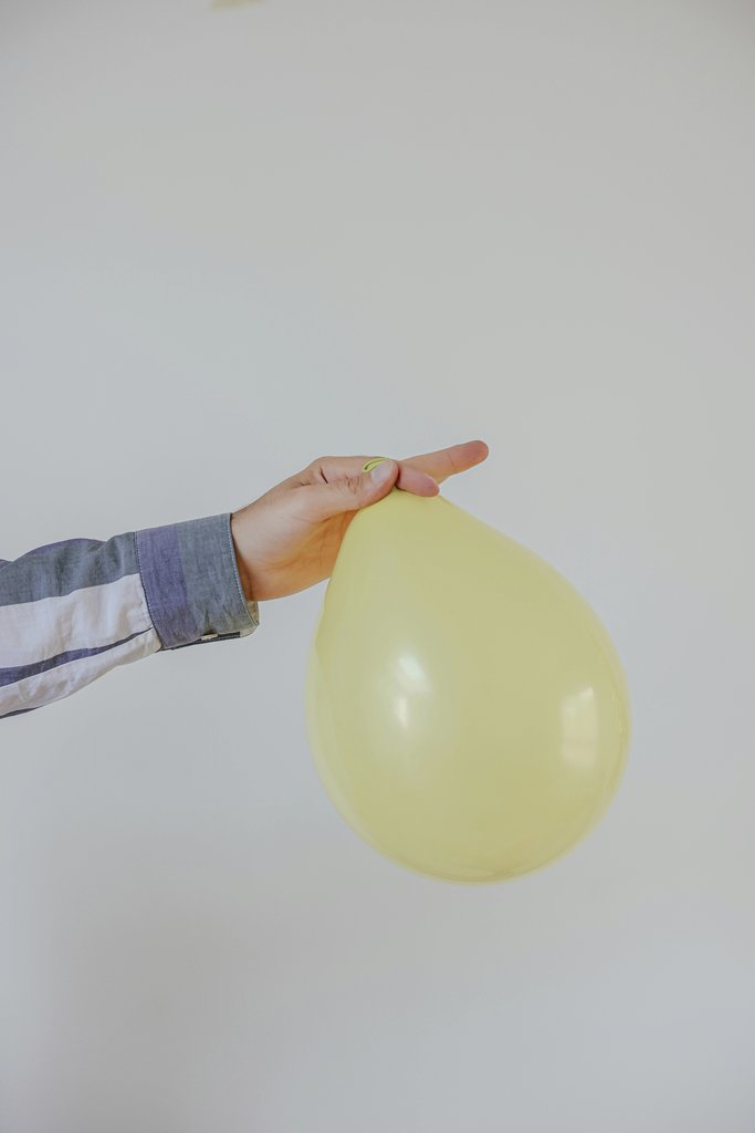 Cup of  Couple - A hand carefully holding a yellow balloon, creating a minimalist and playful composition against a white background.
