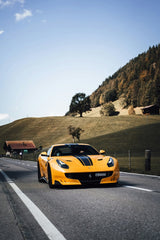 Ferrari F12tdf in Giallo Modena speeding down a road in the Swiss countryside with rolling hills.