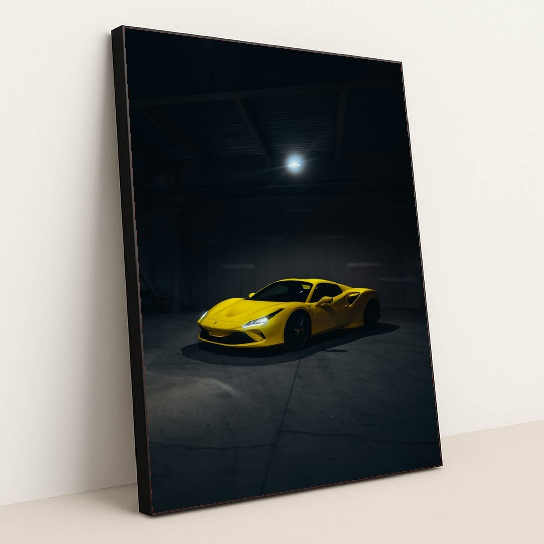 This photo shows a yellow Ferrari sports car spotlighted in a dark, empty garage, in a black frame.