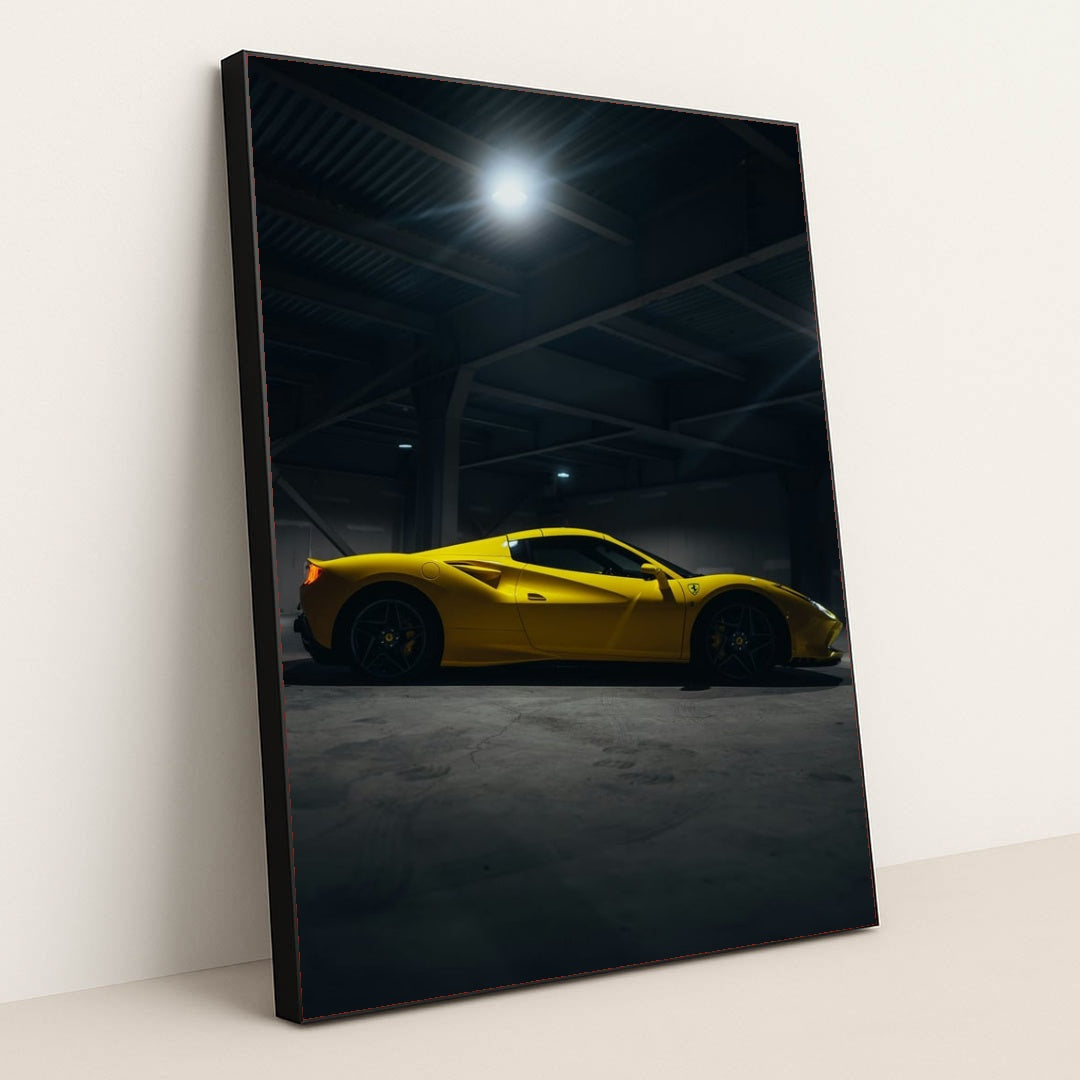 This photo shows a yellow Ferrari sports car in a dimly lit industrial garage, side view captured under overhead lights, in a black frame.