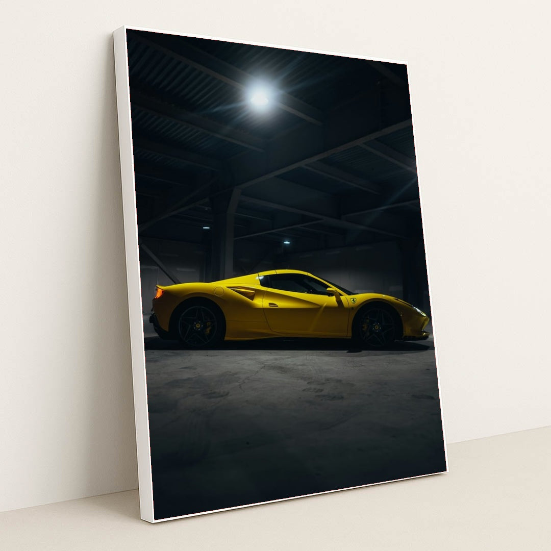 This photo shows a yellow Ferrari sports car in a dimly lit industrial garage, side view captured under overhead lights, in a white frame.