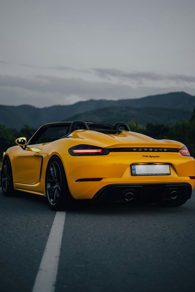 Racing Yellow Porsche 718 Spyder at Dusk on a winding road, showcasing car wall art and stunning alpine scenery.
