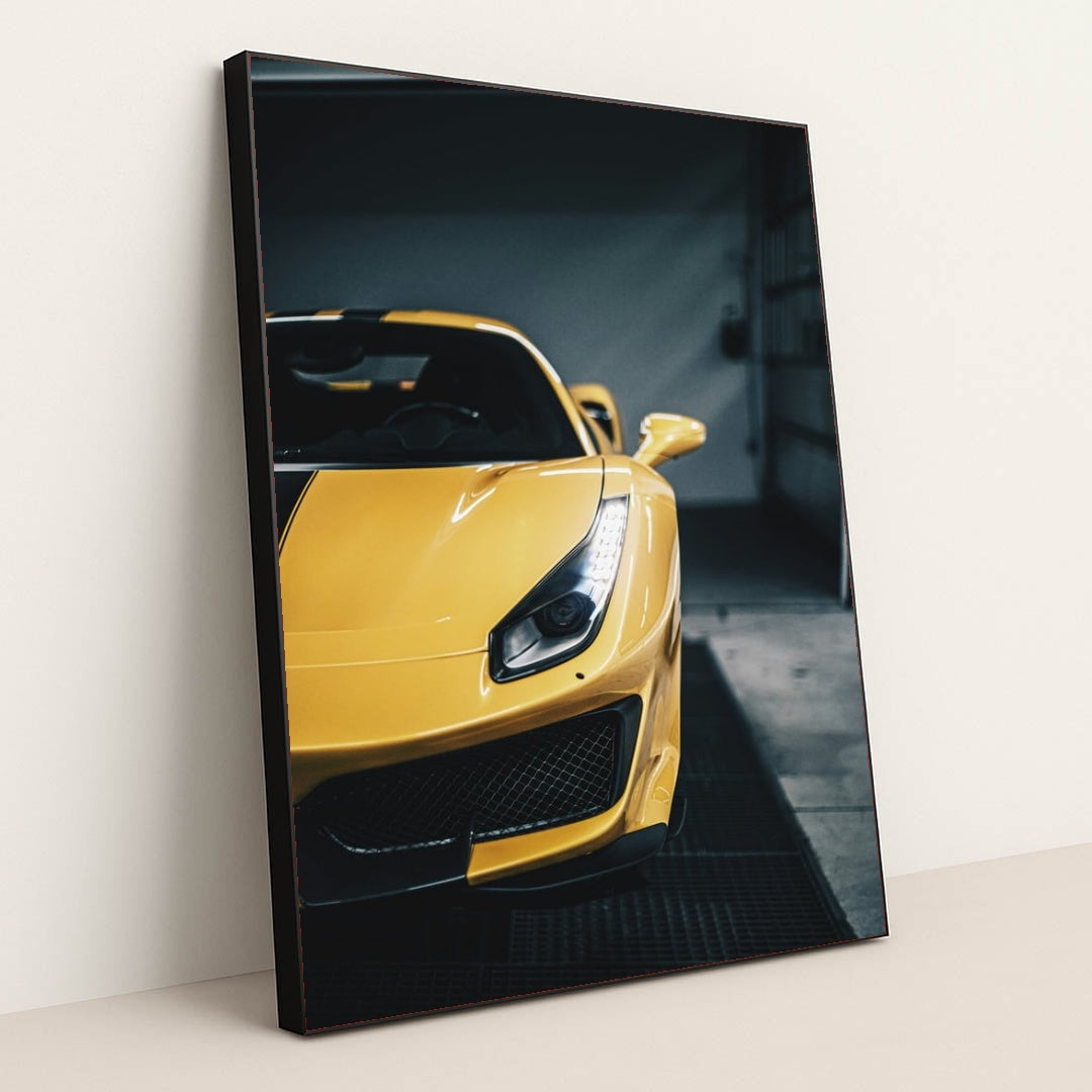 This photo shows the front left side of a yellow Ferrari with sharp headlights and black striping, parked indoors, in a black frame.